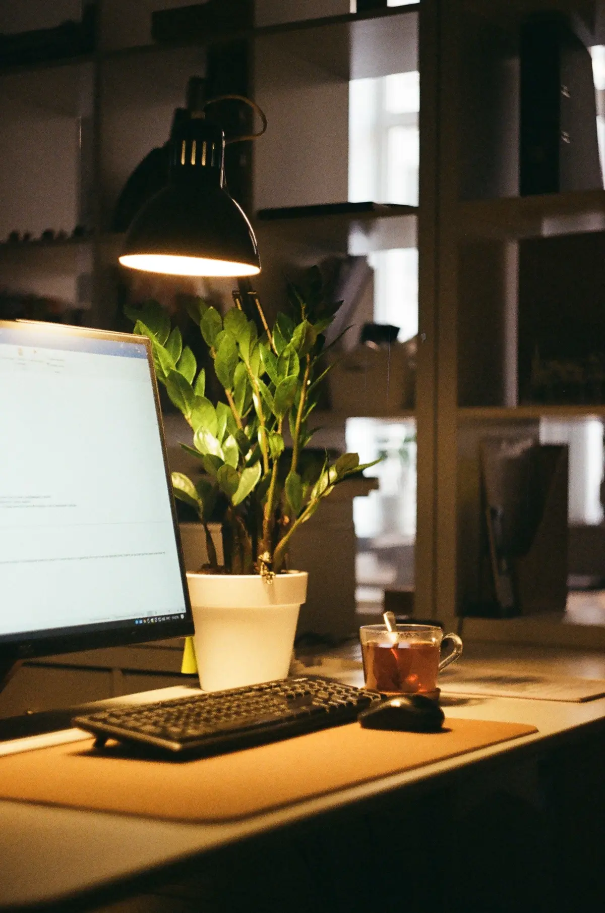 A home desk with a computer monitor, keyboard and lamp