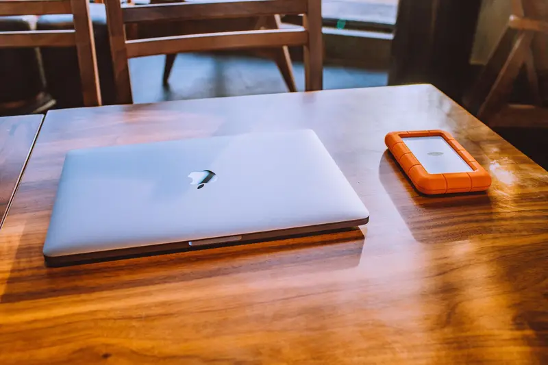 A closed laptop and an orange external hard drive on a wooden table